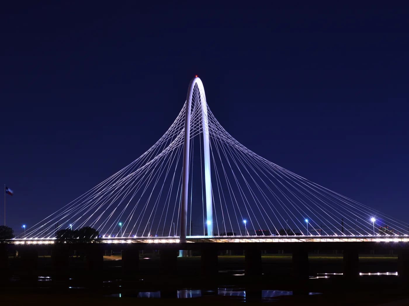 The Margaret Hunt Hill Bridge in Dallas, Texas, lit up at night against a dark sky.